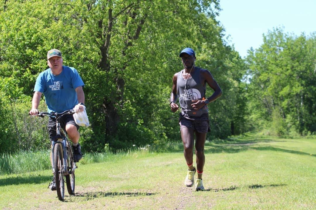 Coree running a wide grass trail beside a cyclist