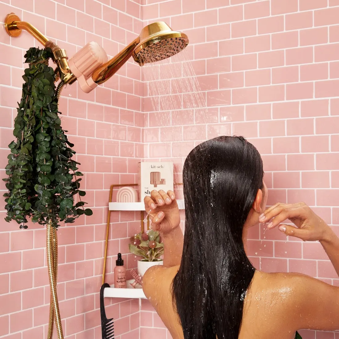 Rinsing hair under a terracotta Kitsch shower filter in a pink tiled shower