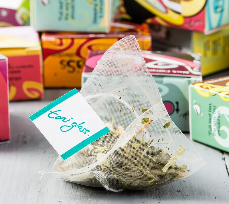 A Toni Glass silken pyramid tea bag resting on its designer boxes