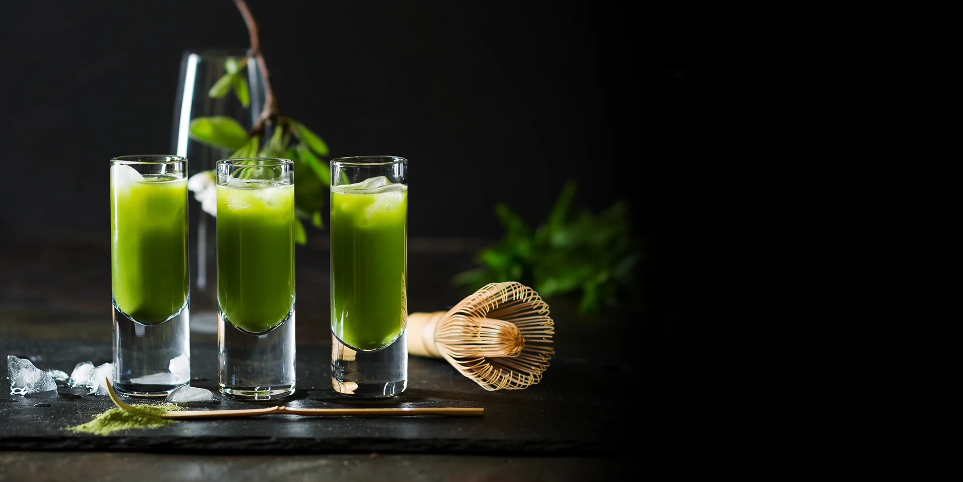Three glasses of bright green Toni Glass Matcha with a bamboo whisk