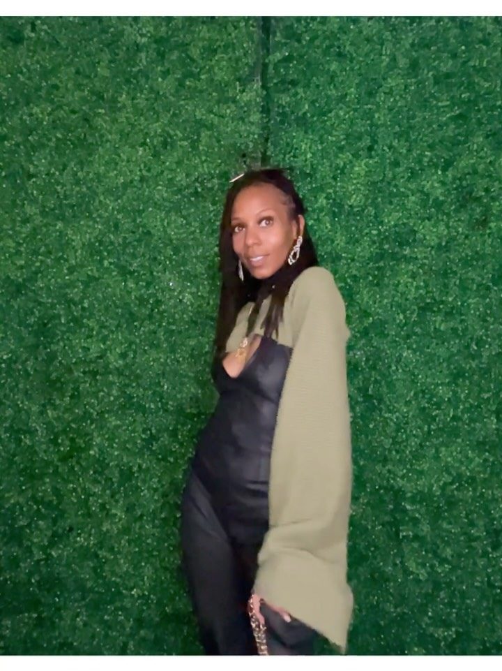 Zsa'Dore in black leather and an olive knit against a green wall